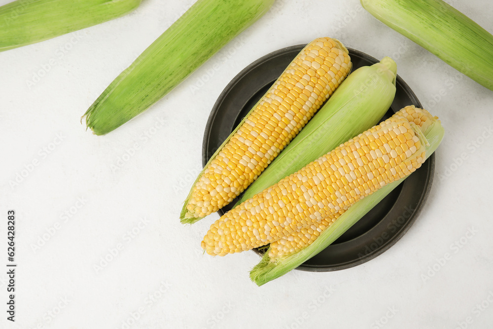 Plate with fresh corn cobs on light background