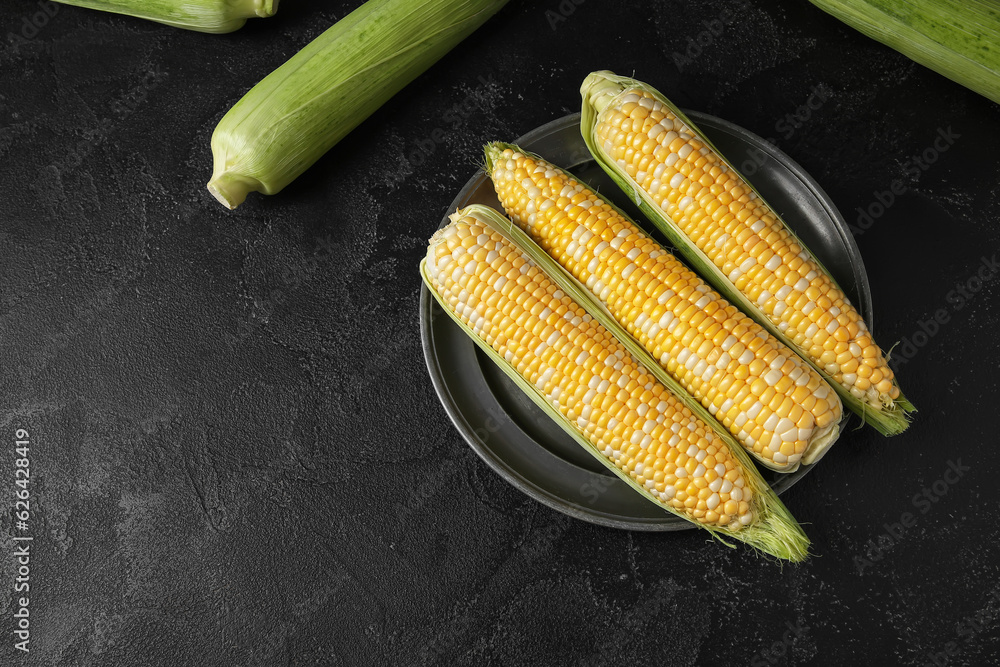 Plate with fresh corn cobs on black background