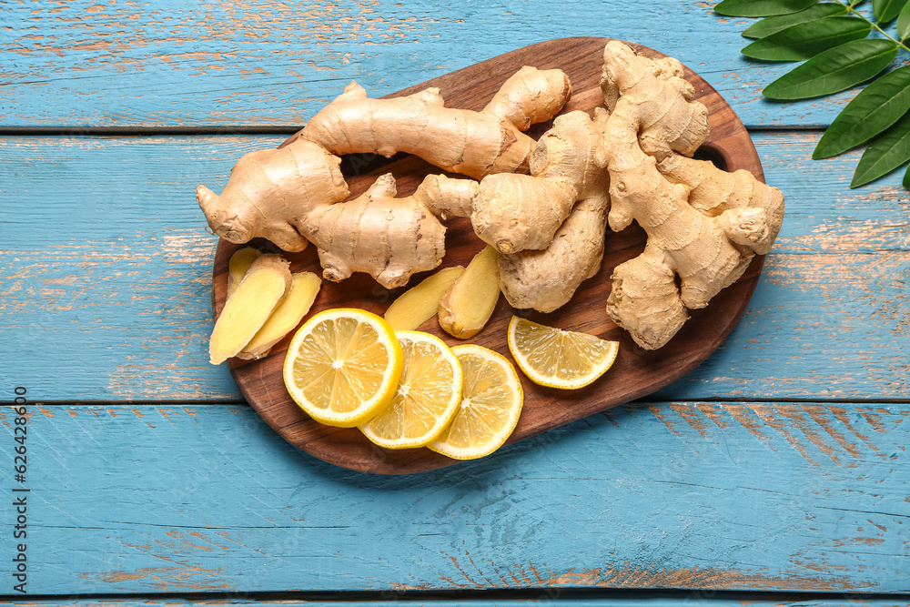 Board with fresh ginger roots and slices of lemon on blue wooden background