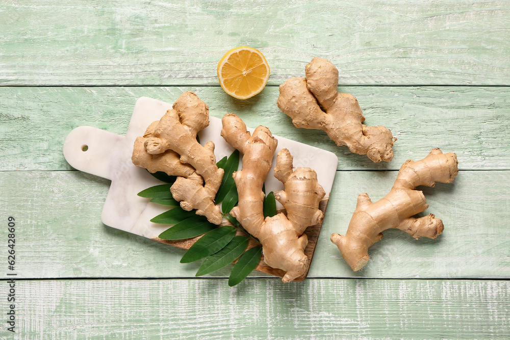 Board with fresh ginger roots, leaves and half of lemon on green wooden background