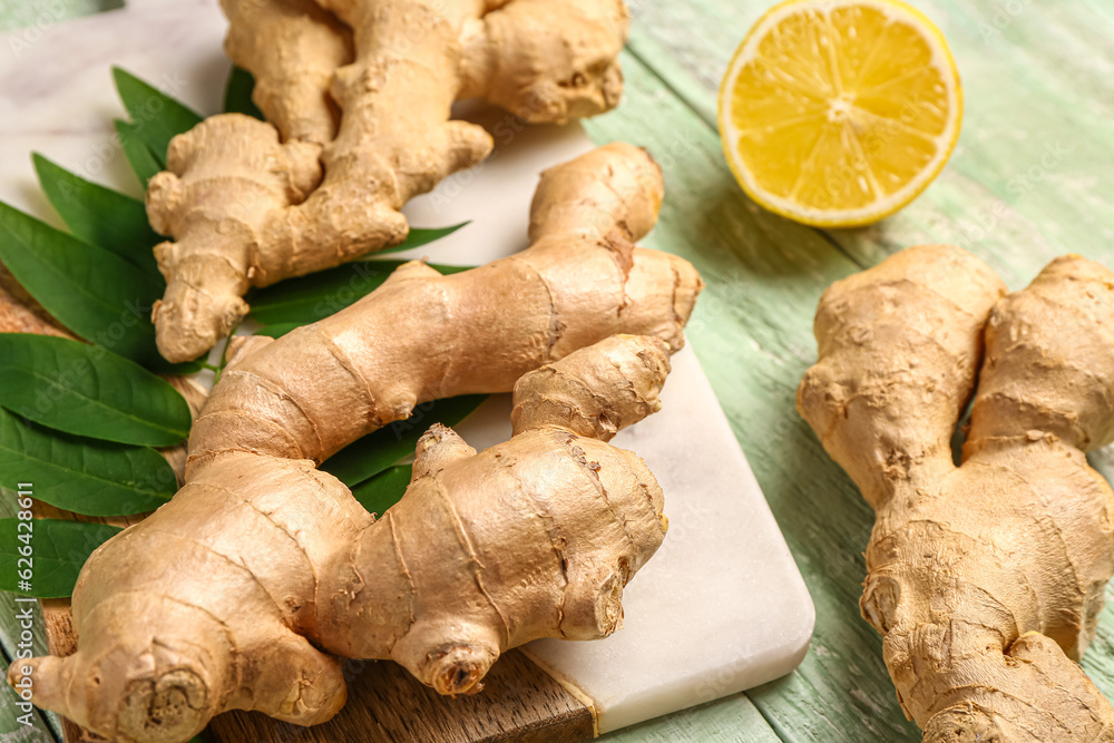 Board with fresh ginger roots, leaves and half of lemon on green wooden background