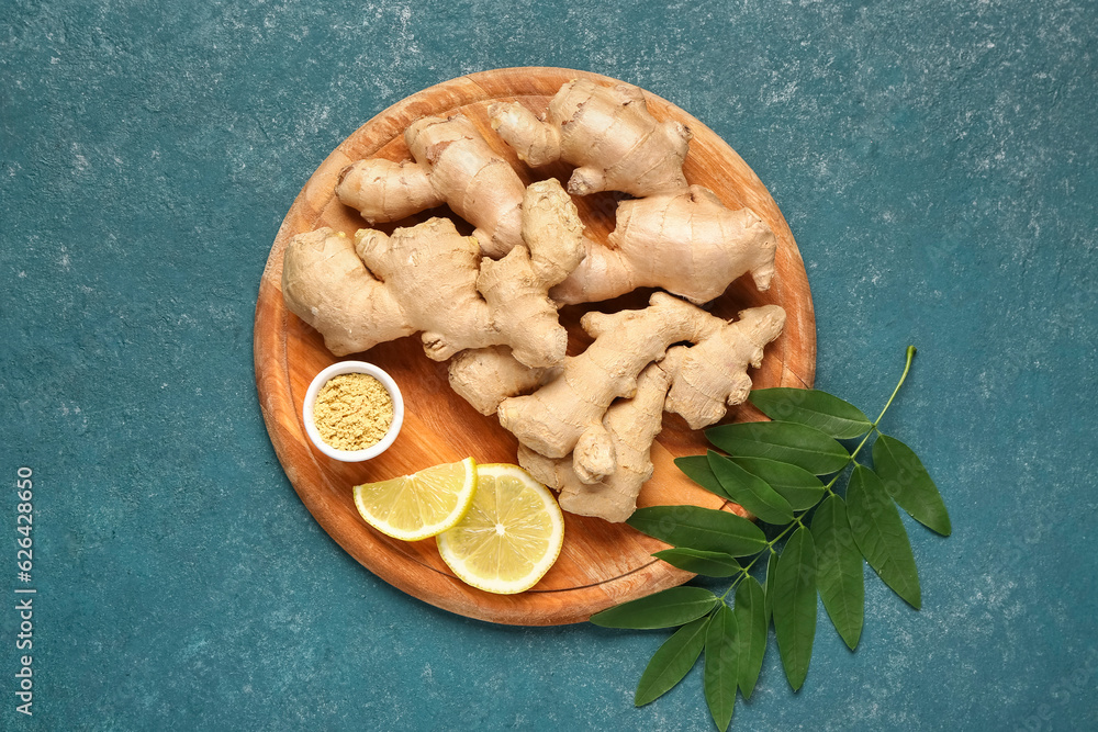 Wooden board with fresh ginger roots, slices of lemon and leaves on blue background