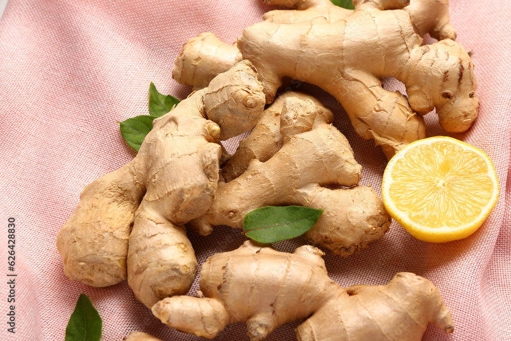 Fresh ginger roots with half of lemon and leaves on napkin, closeup