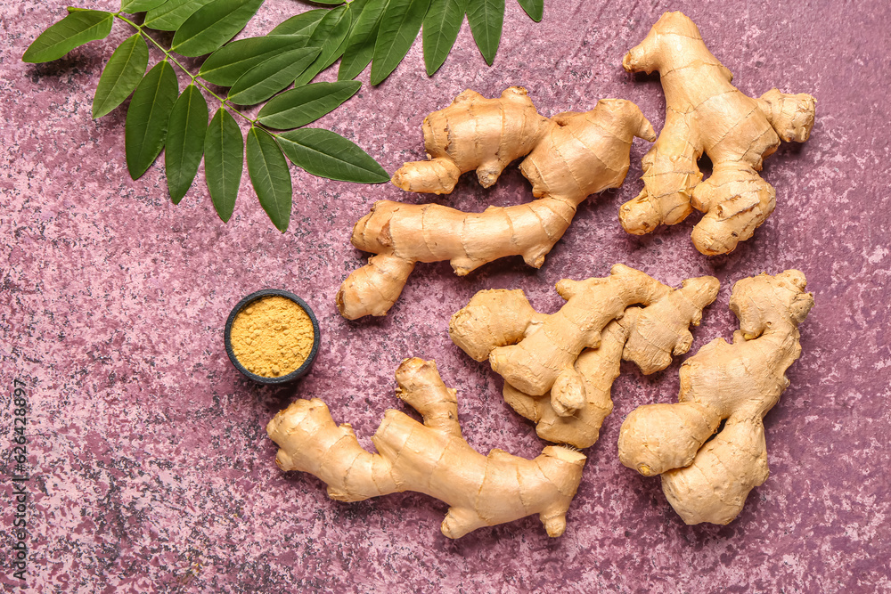 Fresh ginger roots with leaves and bowl of dried powder on purple background