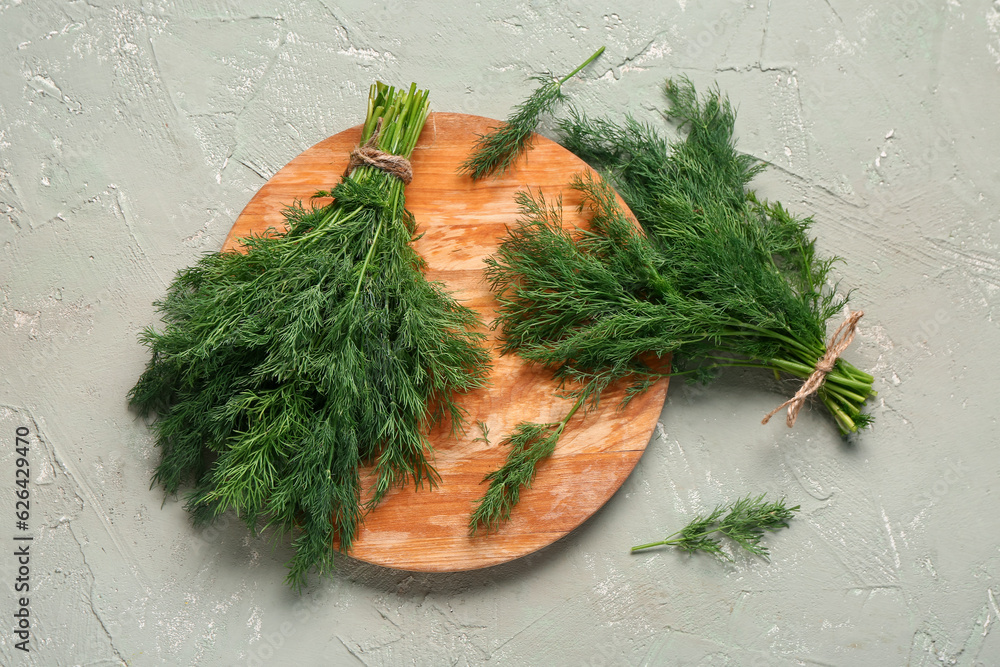 Wooden board with bunches of fresh dill on grey background