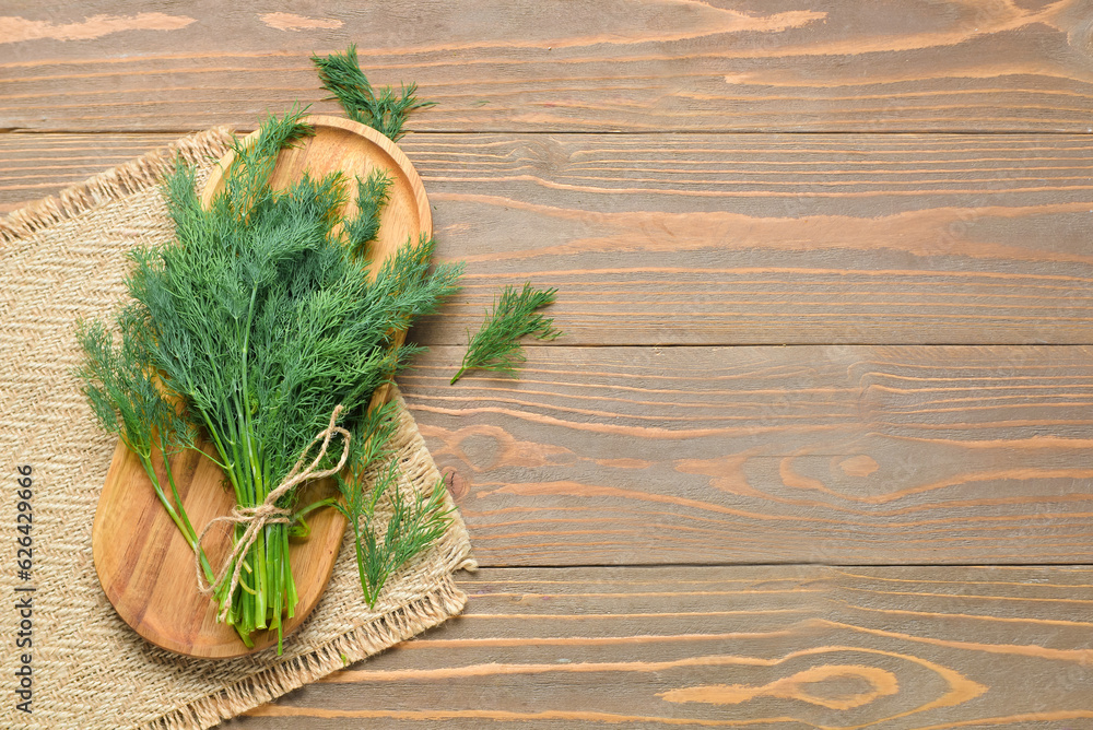 Board with bunch of fresh dill on wooden background