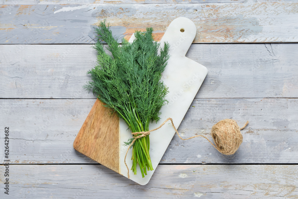 Board with bunch of fresh dill on grey wooden background