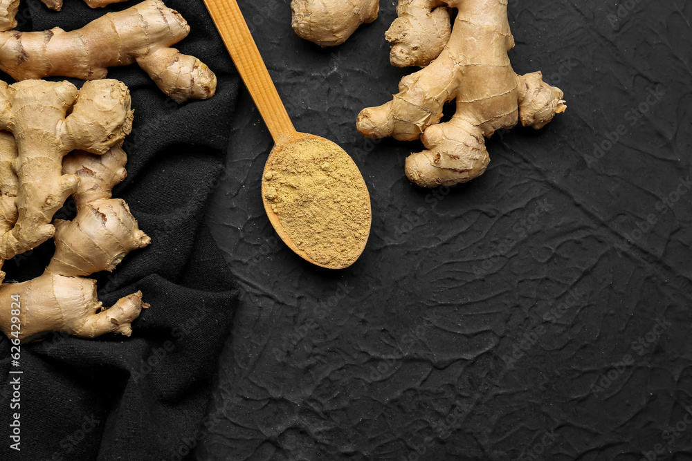 Fresh ginger roots and wooden spoon with dried powder on black background