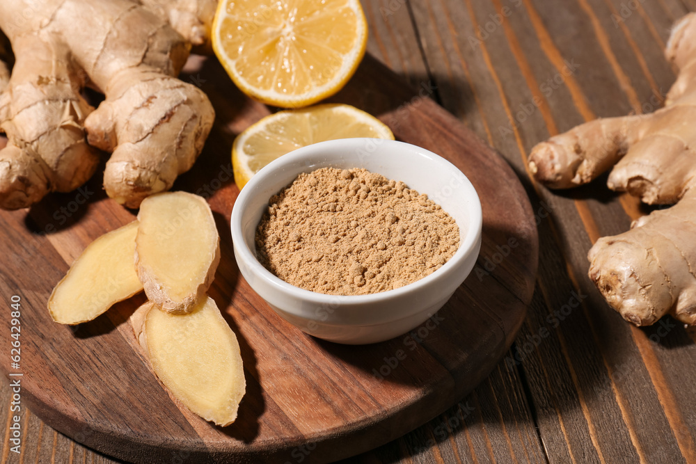 Board with fresh ginger roots, lemon and bowl of dried powder on wooden background