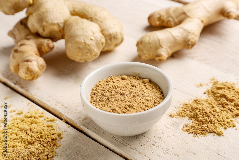 Fresh ginger roots and bowl with dried powder on white wooden background