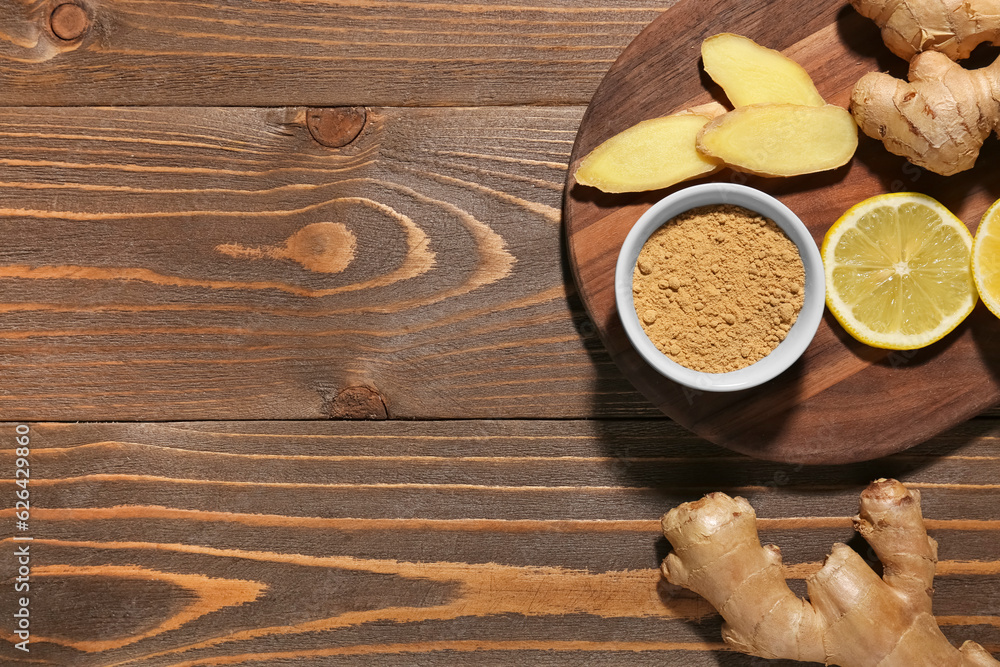 Board with fresh ginger roots, lemon and bowl of dried powder on wooden background