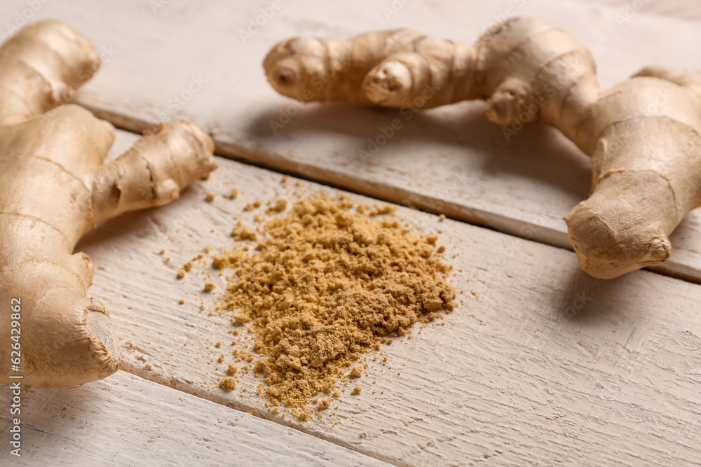 Fresh ginger roots and dried powder on white wooden background