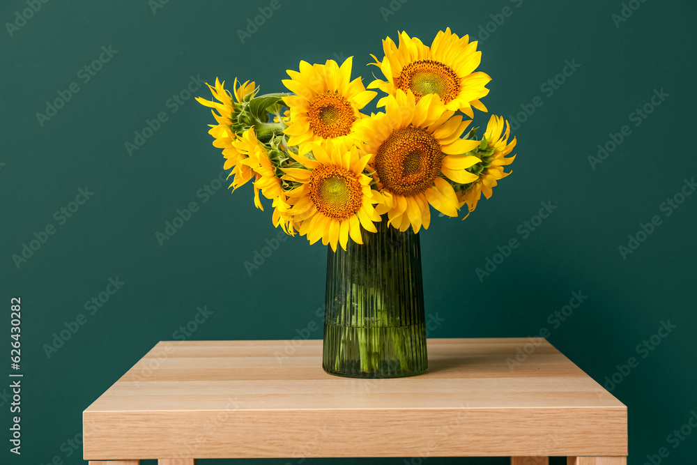 Vase with beautiful sunflowers on table near green wall in room, closeup