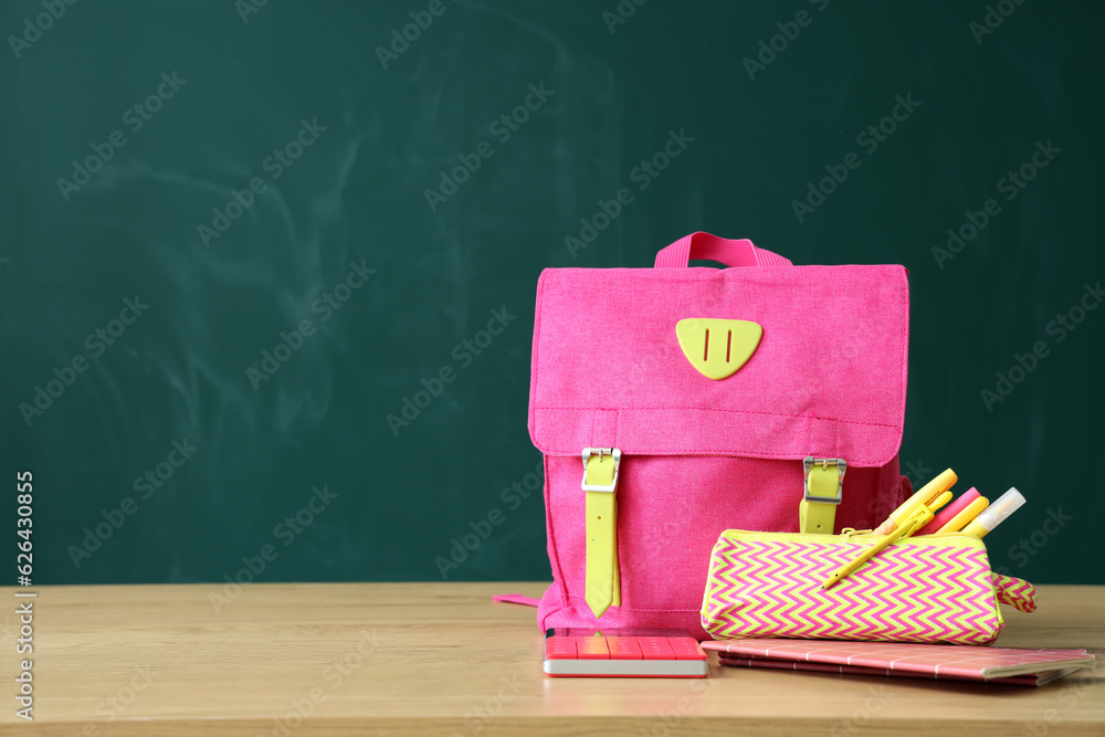 Backpack with school stationery on table near green chalkboard