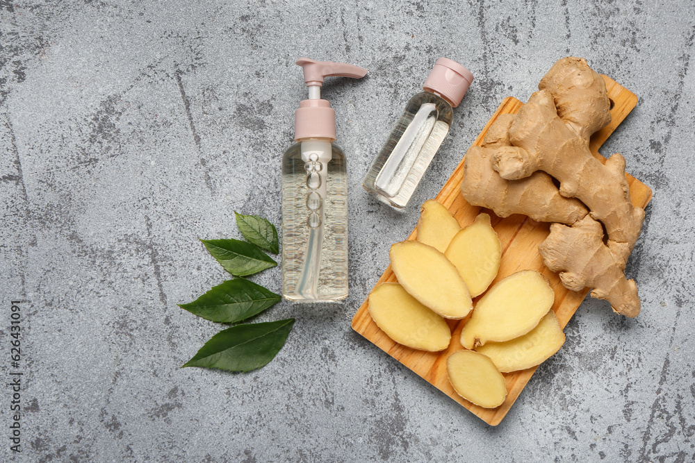 Bottles of cosmetic oil and wooden board with sliced ginger root on grey table