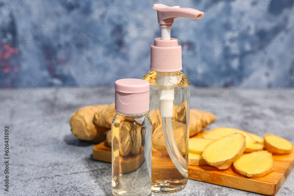 Bottles of cosmetic oil and wooden board with sliced ginger root on grey table