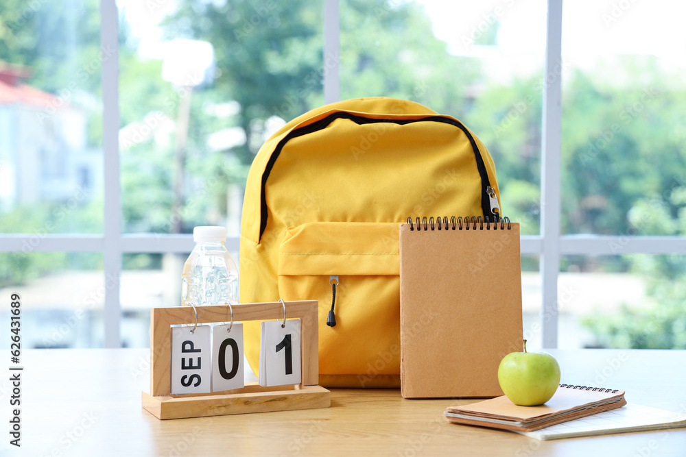 Yellow school backpack with stationery and calendar on brown wooden table near window in classroom