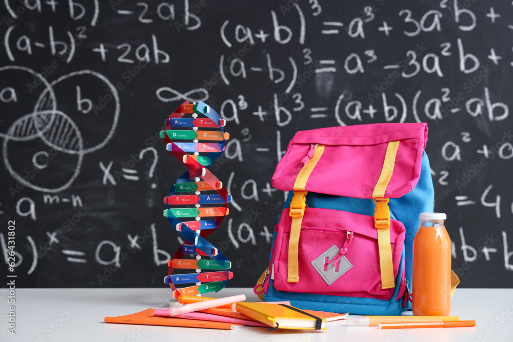 Pink school backpack with stationery, molecular model and bottle of juice on white table near black 