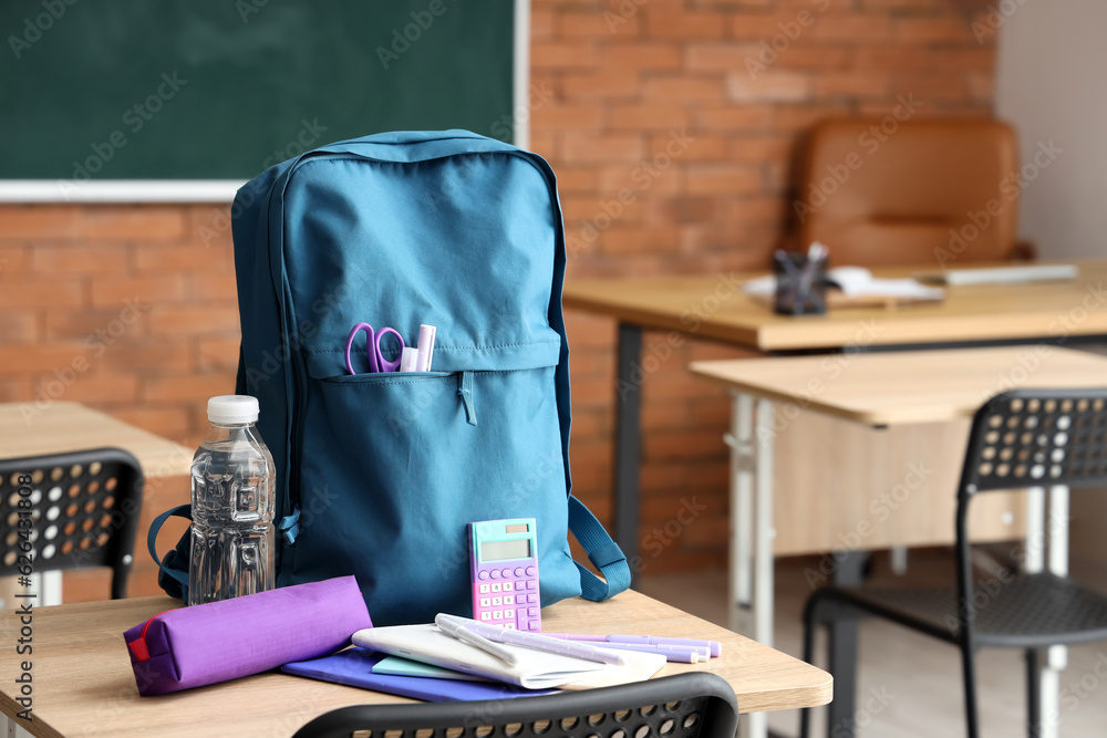 Blue school backpack with stationery and bottle of water on desk in classroom