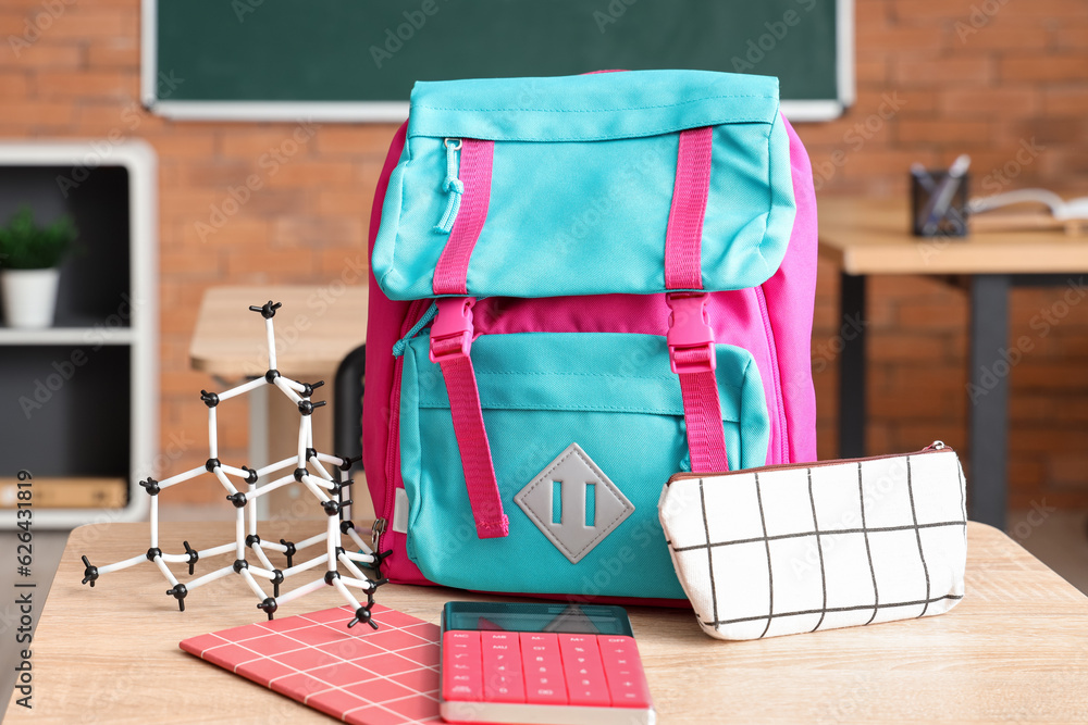 Colorful school backpack with stationery and molecular model on desk in classroom