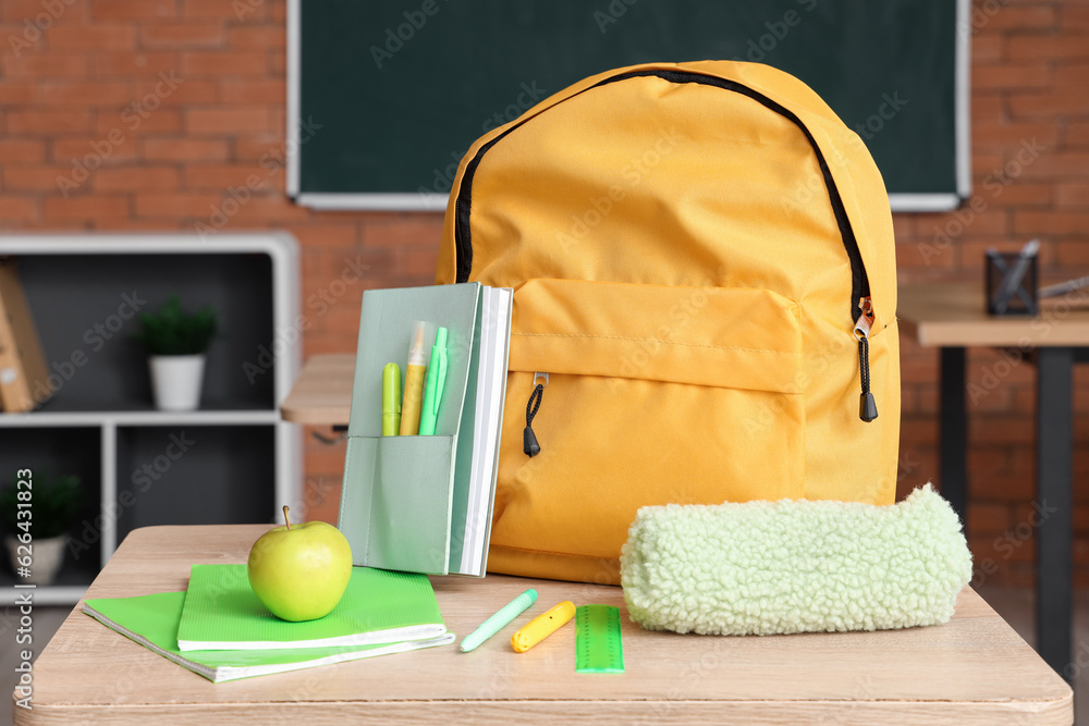 Yellow school backpack with stationery and fresh apple on desk in classroom