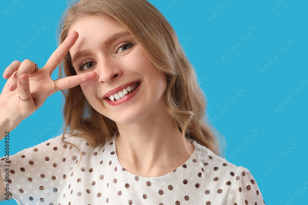 Young woman showing victory gesture on blue background, closeup