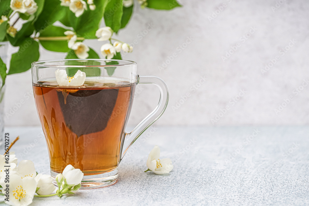 Cup of aromatic tea and beautiful jasmine flowers on light background