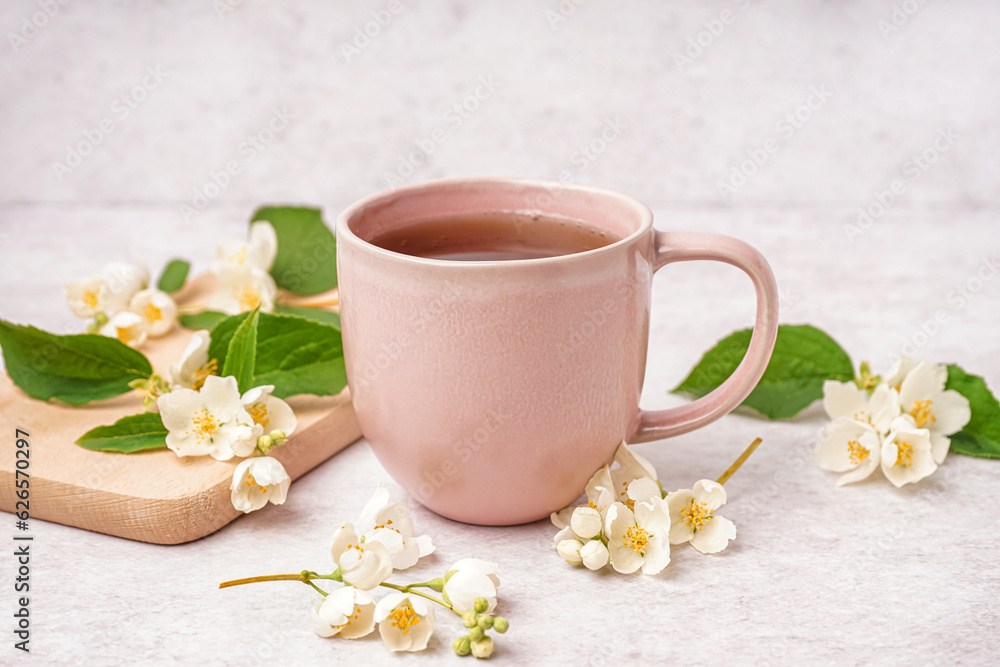 Cup of tasty tea and beautiful jasmine flowers on light background