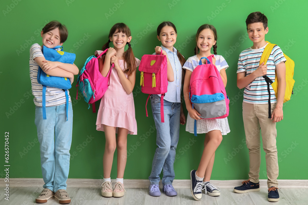 Little pupils with backpacks near green wall