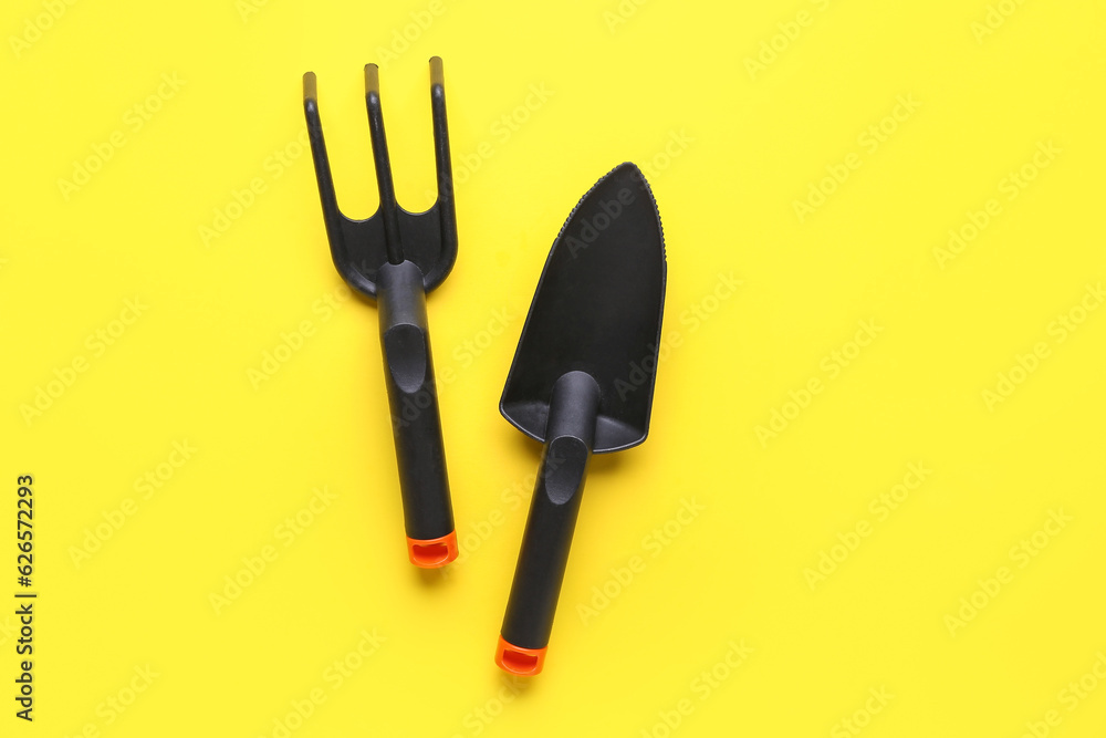 Gardening rake and shovel on yellow background