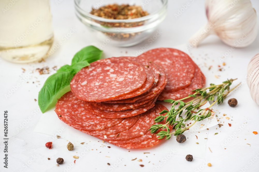 Slices of tasty salami on light background