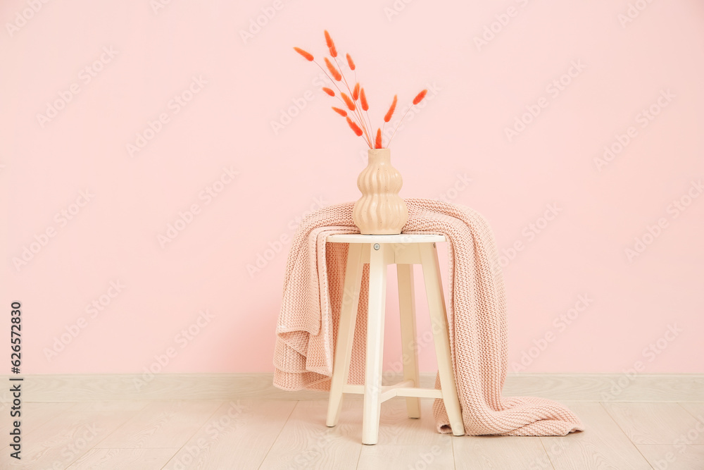 Vase with dried flowers and blanket near pink wall