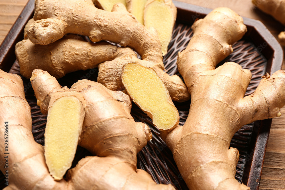 Tray with fresh ginger roots on wooden background