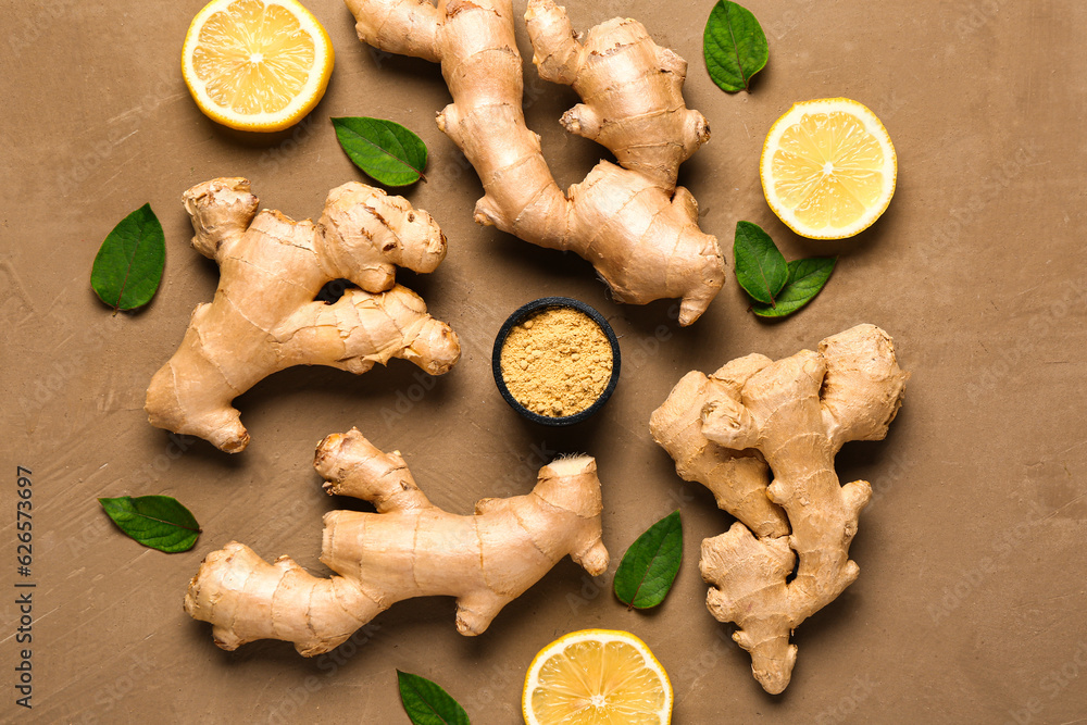 Fresh ginger roots with sliced lemon, leaves and bowl of dried powder on brown background