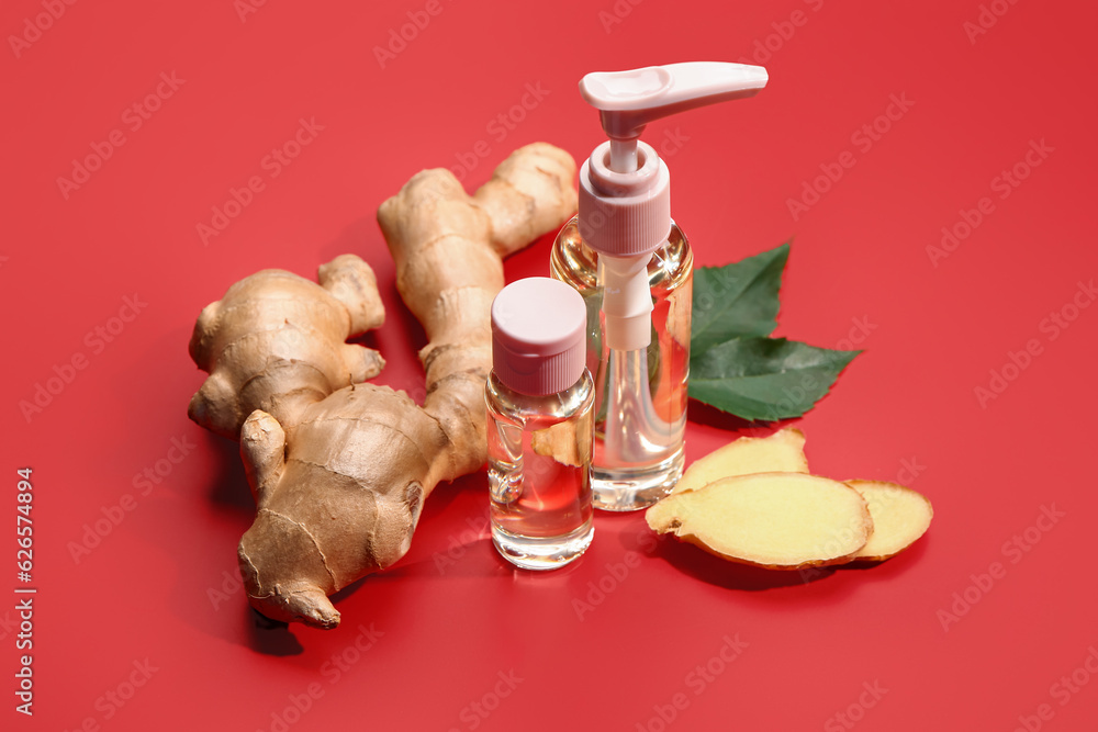 Bottles of ginger cosmetic oil and leaves on red background