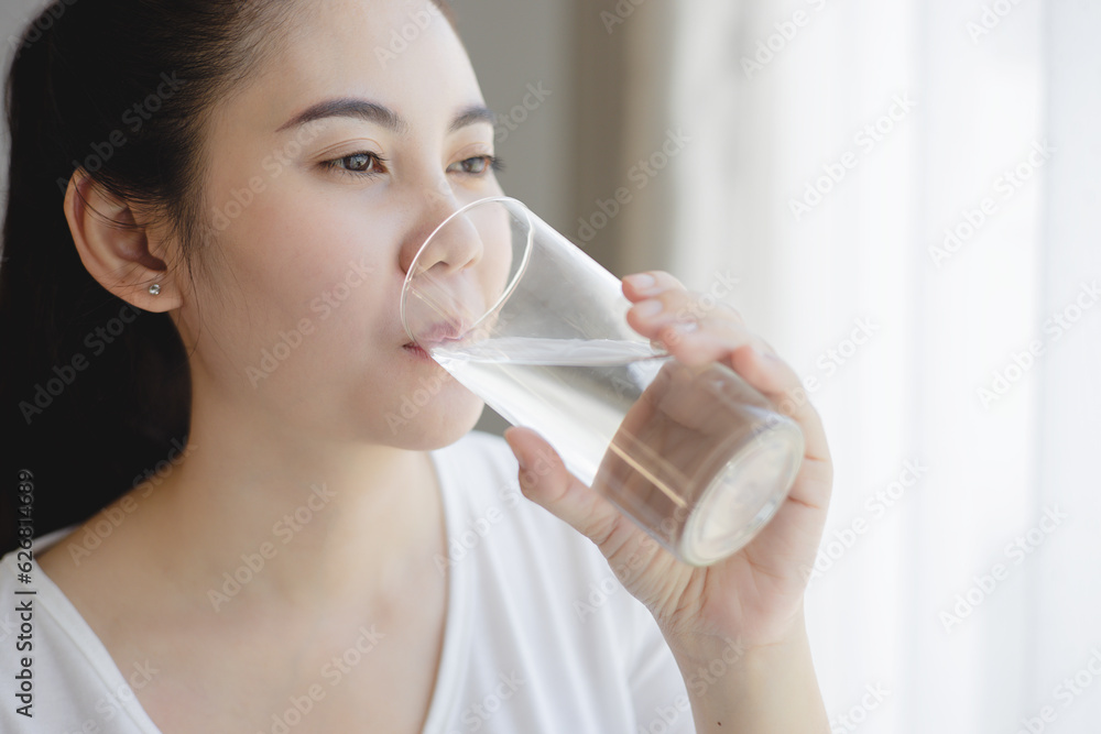 Healthy beautiful Asian young woman drinking pure water from glass at home. Caucasian female model h