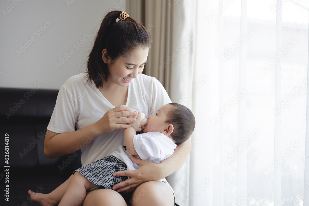 Asian young mother holding and feeding baby from milk bottle at living home. loving woman giving dri