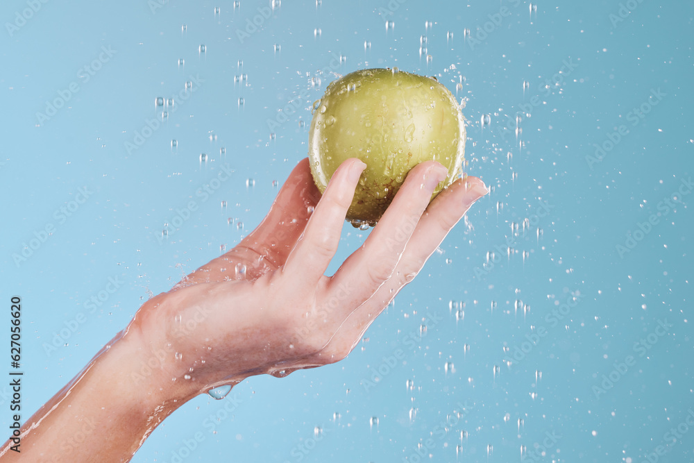 Apple, cleaning and hand with water drops for wellness and skincare in a studio. Isolated, blue back