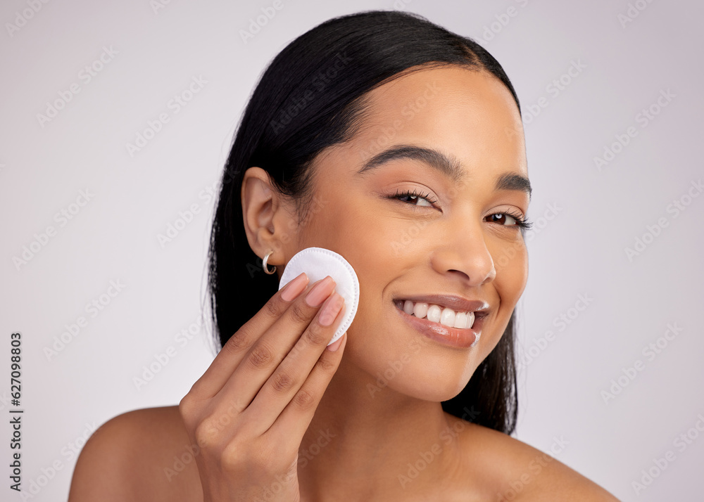 Happy woman, cotton pad and cleaning face in skincare for makeup removal against a grey studio backg