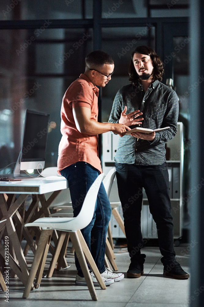 Hes giving me some really cool ideas. Shot of two businessmen discussing in a notebook while working