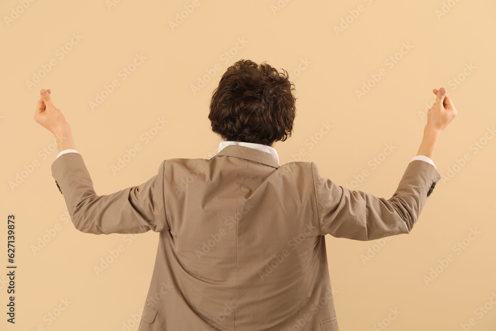 Young man making heart with his fingers on beige background, back view