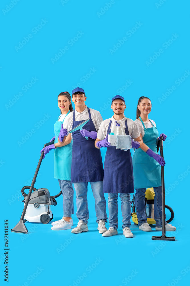 Young janitors with cleaning supplies on blue background