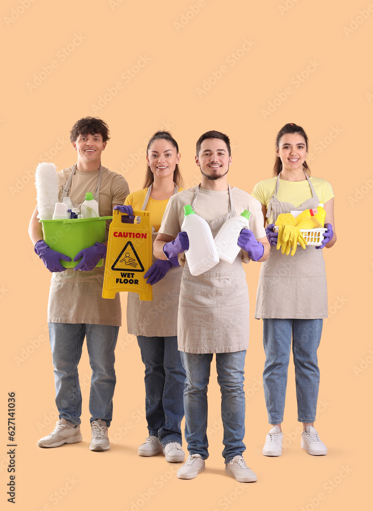 Young janitors with cleaning supplies on beige background