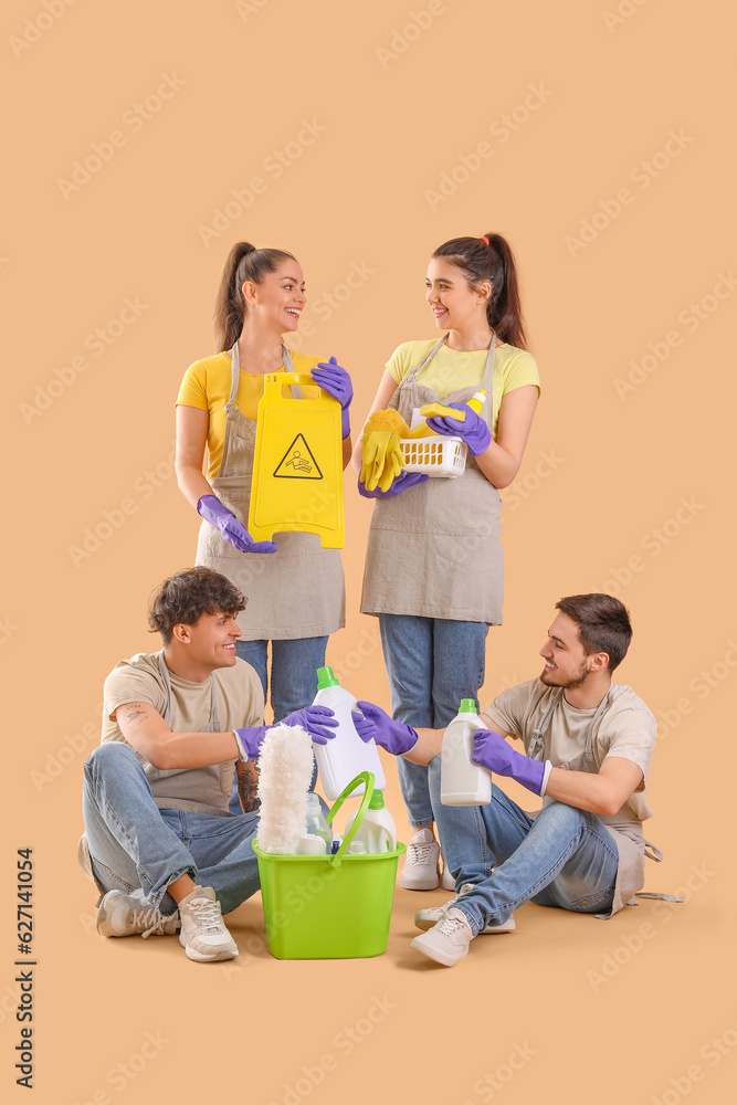 Young janitors with cleaning supplies on beige background