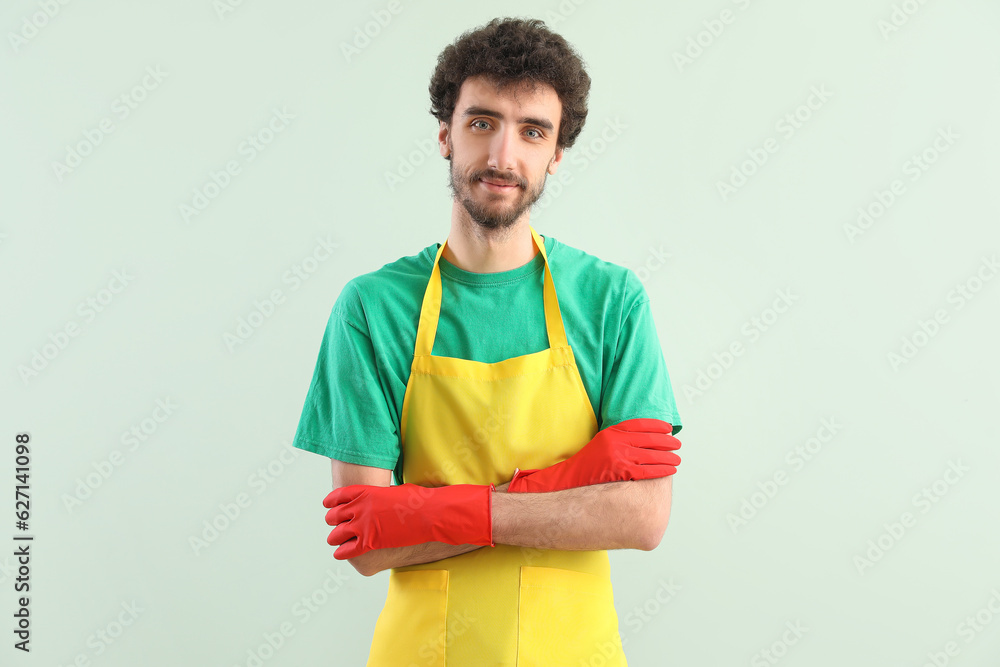 Young man in rubber gloves and apron on green background