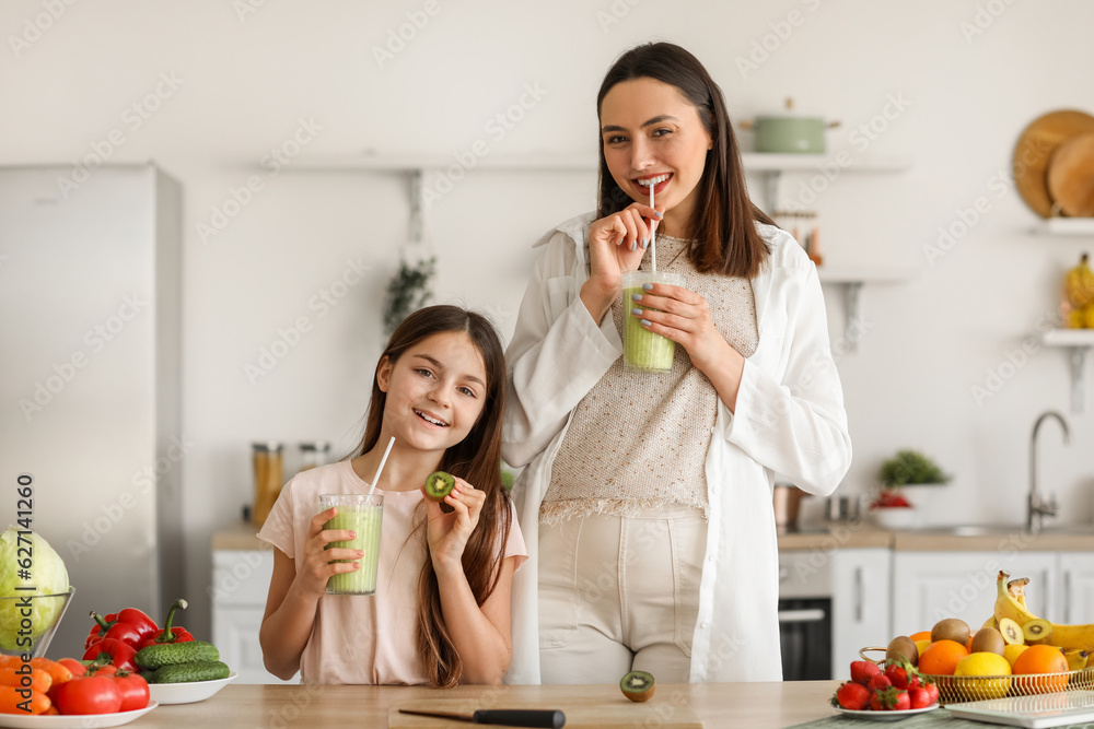 Little girl with her pregnant mother drinking green smoothie in kitchen