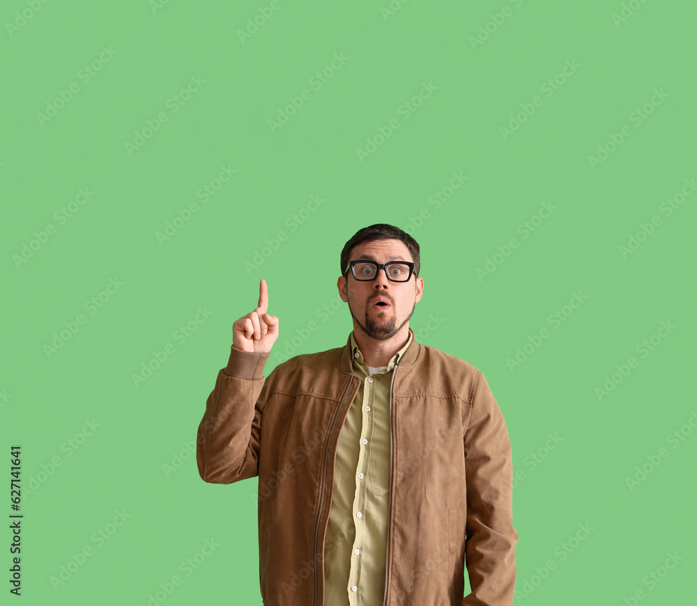 Handsome man in stylish eyeglasses pointing at something on green background