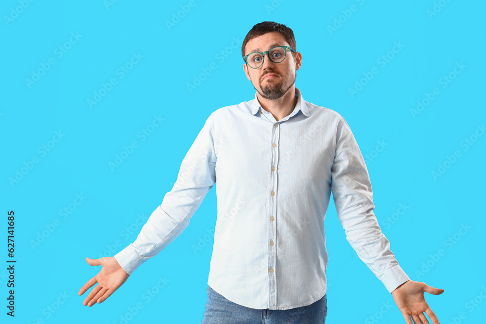 Handsome man in stylish eyeglasses shrugging on blue background