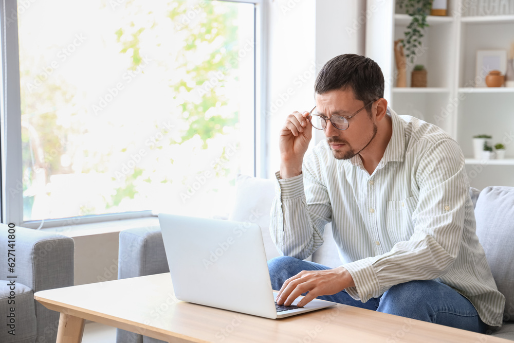 Handsome man in stylish eyeglasses using laptop at home