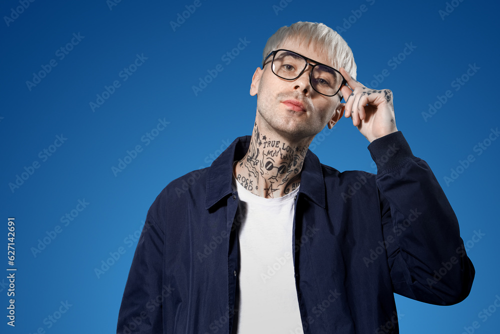 Young tattooed man in eyeglasses on blue background